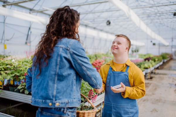 A happy young employee with Down syndrome working in garden centre, taking payment from customer.