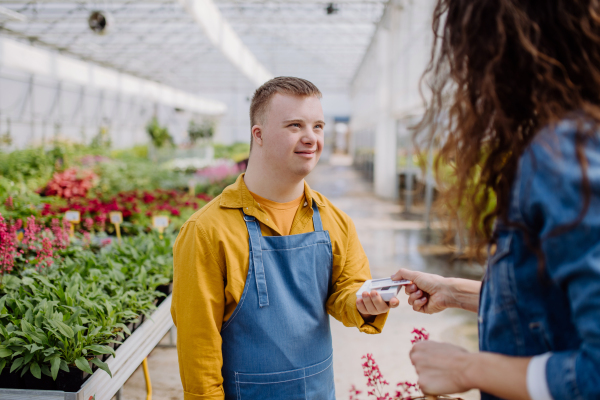 A happy young employee with Down syndrome working in garden centre, taking payment from customer.