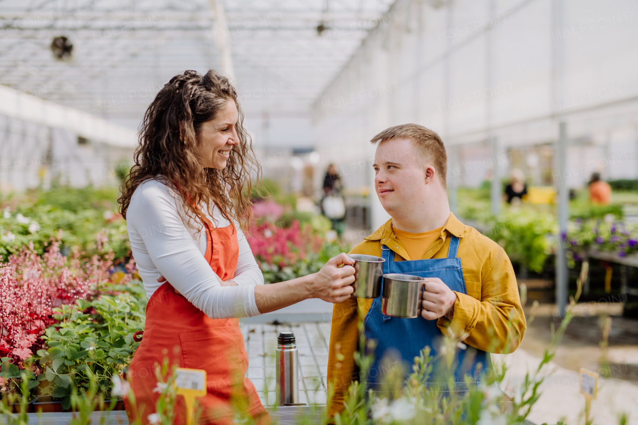 A woman florist with her young colleague with Down syndrome having tea break in garden centre.