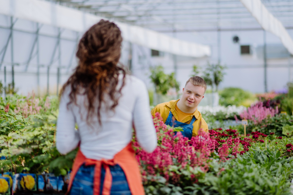 An experienced woman florist helping young employee with Down syndrome in garden centre.