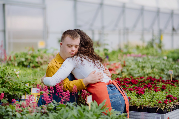 A woman florist hugging her young colleague with Down syndrome in garden centre.