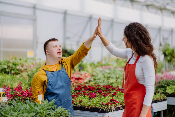 An experienced woman florist helping young employee with Down syndrome in garden centre.