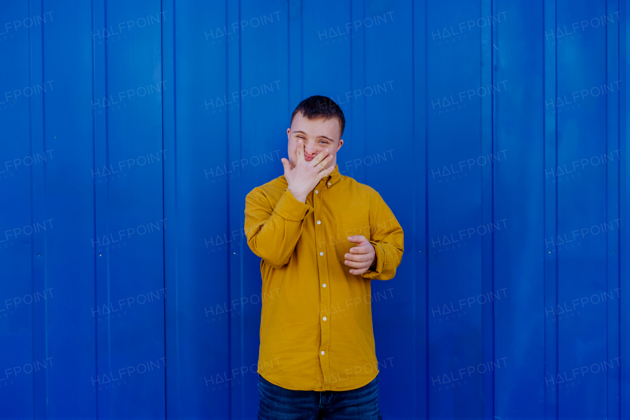 A happy young man with Down syndrome smiling and looking at camera against blue background.