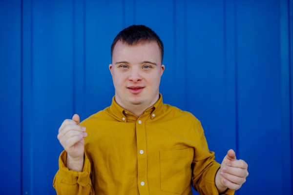 A happy young man with Down syndrome smiling and looking at camera against blue background.