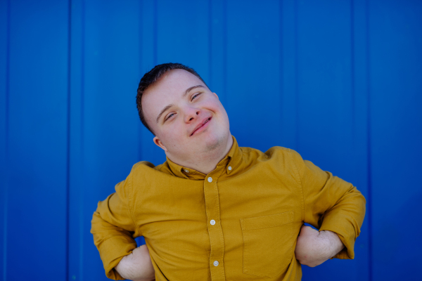 A happy young man with Down syndrome smiling and looking at camera against blue background.