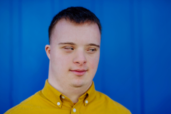 A portrait of happy young man with Down syndrome smiling against blue background.