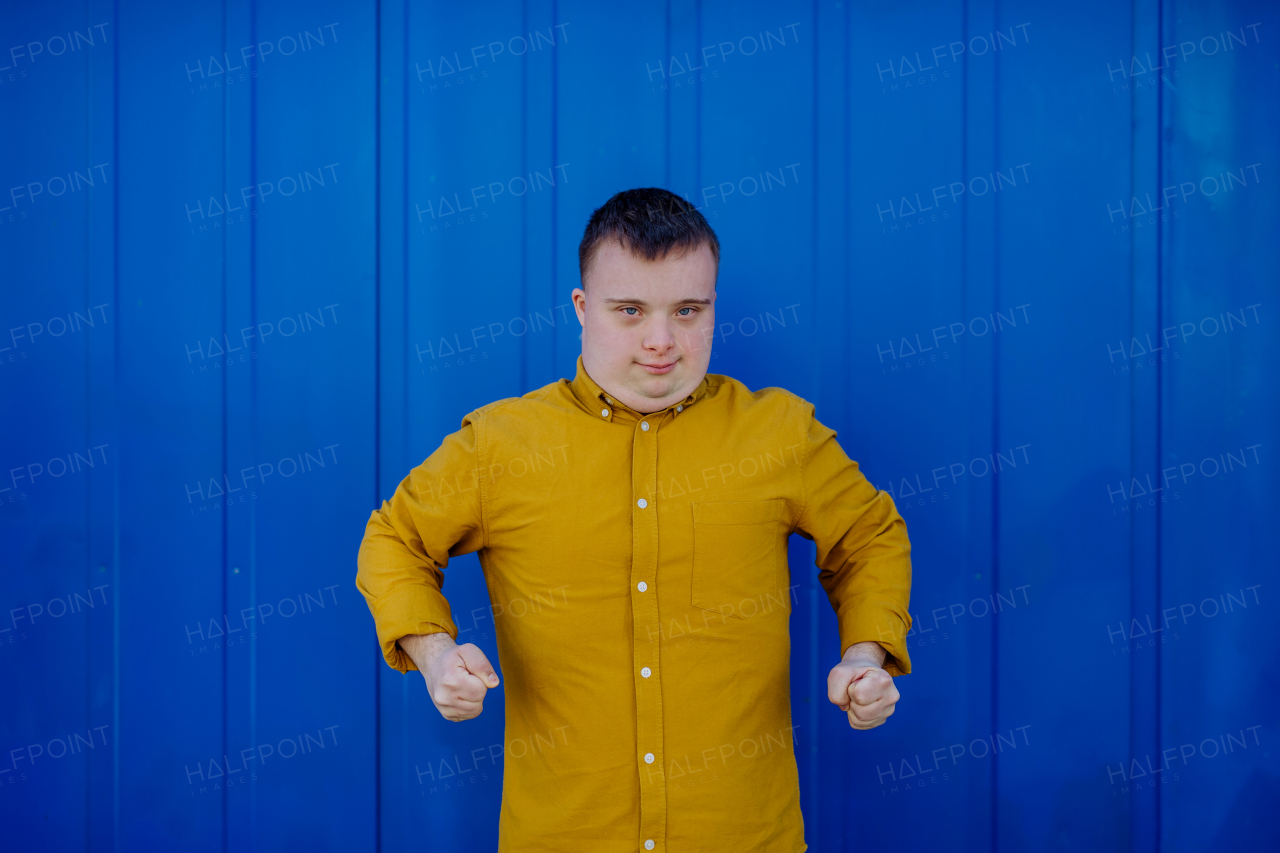 A happy young man with Down syndrome smiling and looking at camera against blue background.