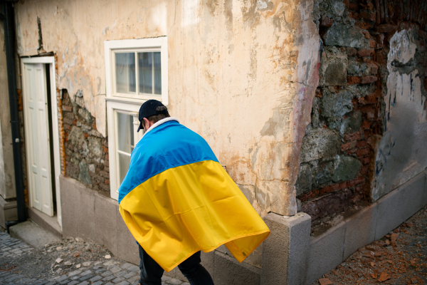 A protestor covered with blue and yellow Ukrainian flag protesting against war in Ukraine in street