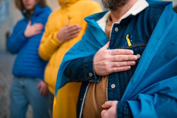 A cropped shot of protestors with Ukrainian blue and yellow ribbons and flags protesting against war in Ukraine in street