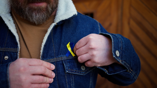 A close-up of protestor pinning Ukrainian blue and yellow ribbon protesting against war in Ukraine in street