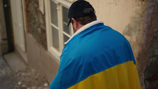 A protestor covered with blue and yellow Ukrainian flag protesting against war in Ukraine in street