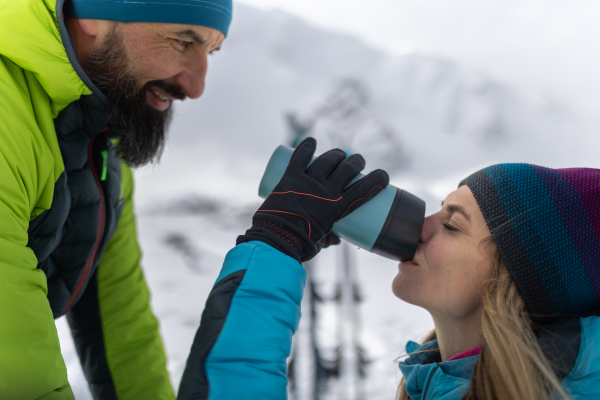 Ski touring couple having break, drinking tea from a thermos during hiking up a mountain in the Low Tatras in Slovakia.