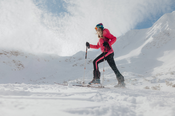 A female backcountry skier hiking to the summit of a snowy peak in the Low Tatras in Slovakia.