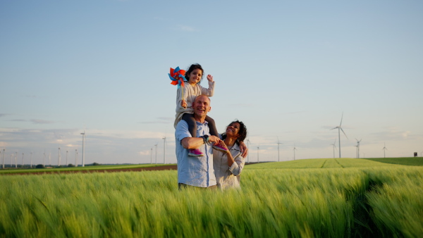 A multiracial family going for walk in field between wind turnines, concept of ecology and alternative energy