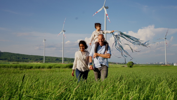 A multiracial family going for walk in field between wind turnines, concept of ecology and alternative energy