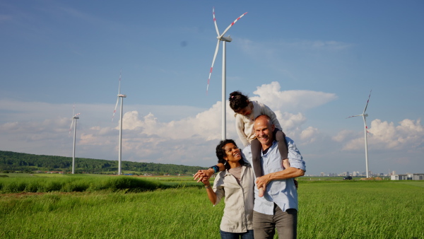 A multiracial family going for walk in field between wind turnines, concept of ecology and alternative energy