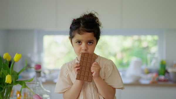 A little girl eating bar of chocolate at home.