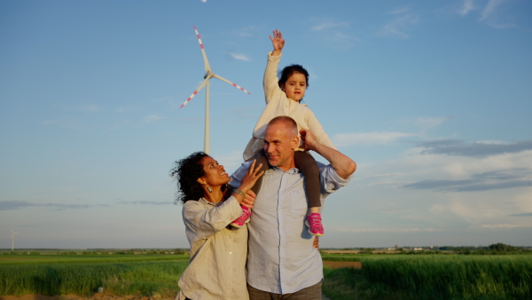 A multiracial family going for walk in field between wind turnines, concept of ecology and alternative energy