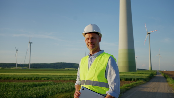 An engineer man standing in front of wind turbines generating electricity power station. Concept of sustainability development by alternative energy