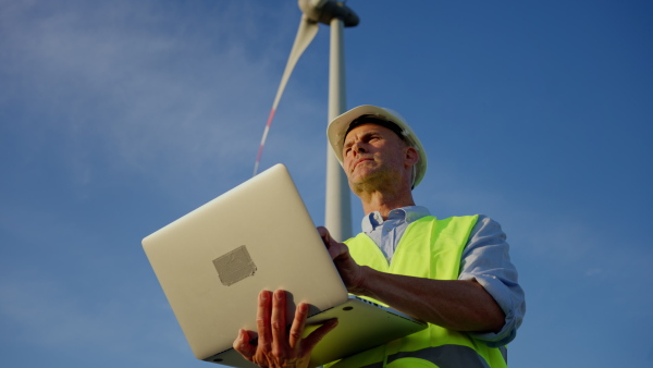 An engineer man standing in front of wind turbines generating electricity power station. Concept of sustainability development by alternative energy