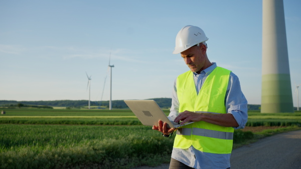 An engineer man standing in front of wind turbines generating electricity power station. Concept of sustainability development by alternative energy