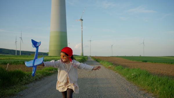 A little girl playing with toy plane in wind turbine field, alternative energy concept.