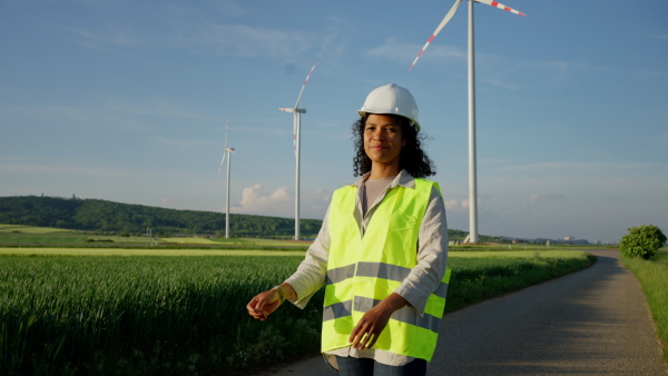 An engineer woman standing in front of wind turbines generating electricity power station. Concept of sustainability development by alternative energy