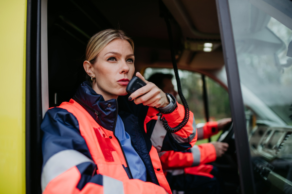 Portrait of a young woman doctor sitting and talking in to walkie-talkie in ambulance car.