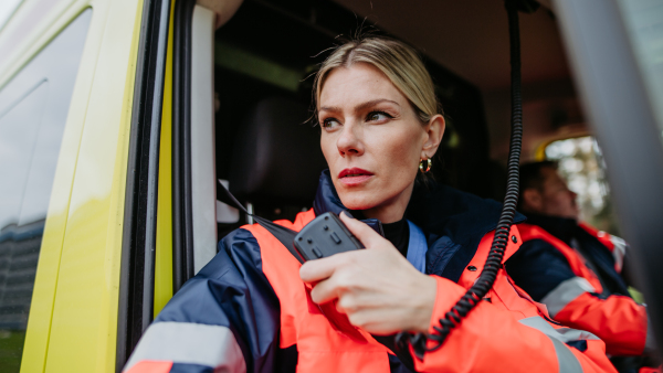 Portrait of a young woman doctor sitting and talking in to walkie-talkie in ambulance car.