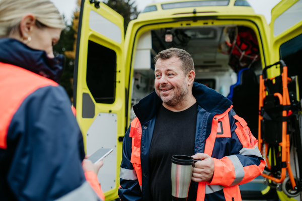 Rescuers having break in front of an ambulance car, talking and drinking coffee.