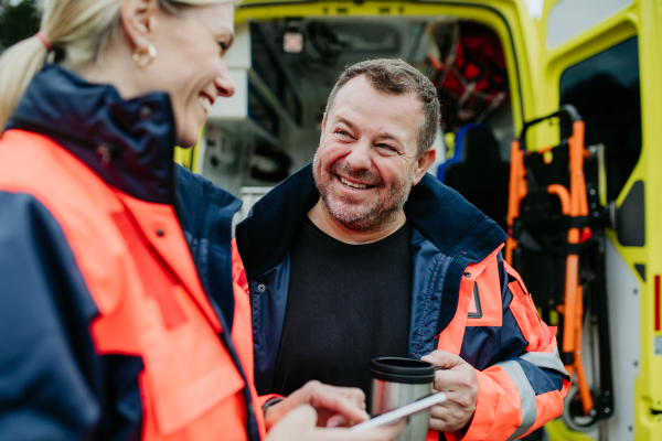 Rescuers having break in front of an ambulance car, talking and drinking coffee.