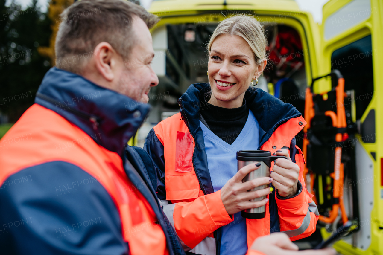 Rescuers having break in front of an ambulance car, talking and drinking coffee.