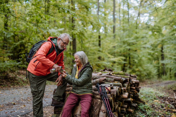 Senior couple having a break during hiking in autumn forest.