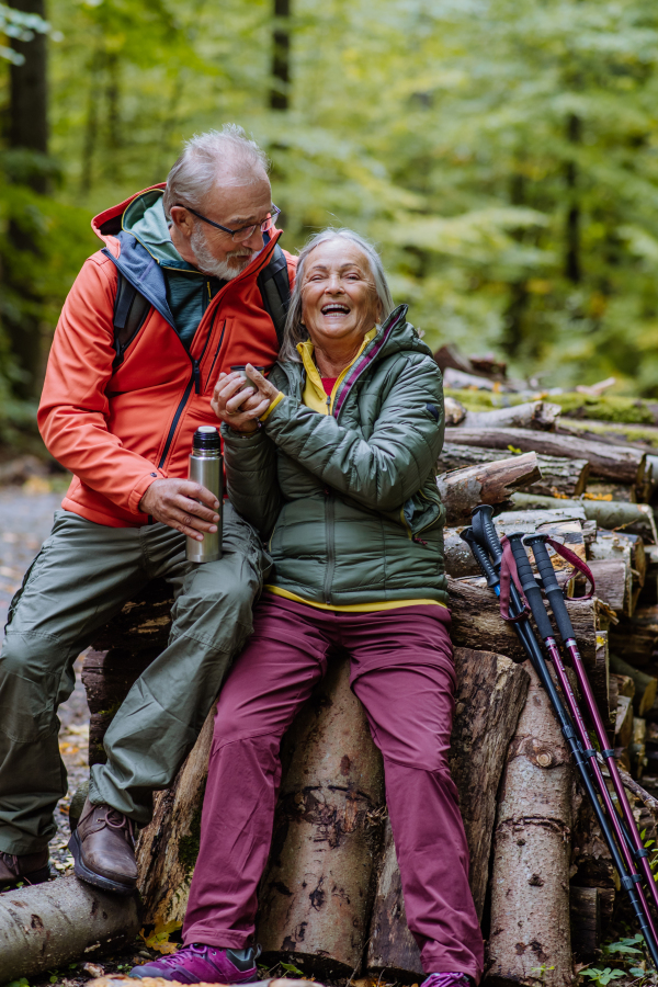 Senior couple having a break during hiking in autumn forest.