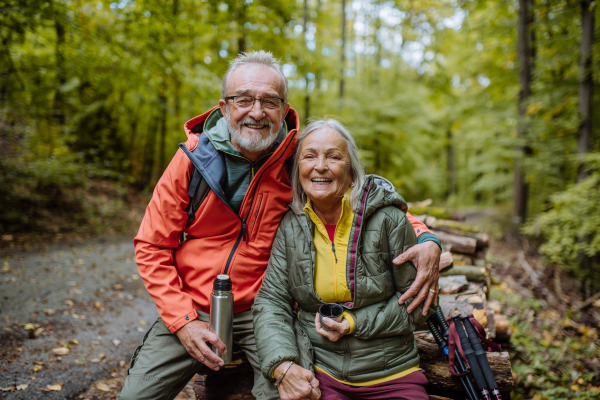 Senior couple having a break during hiking in autumn forest.