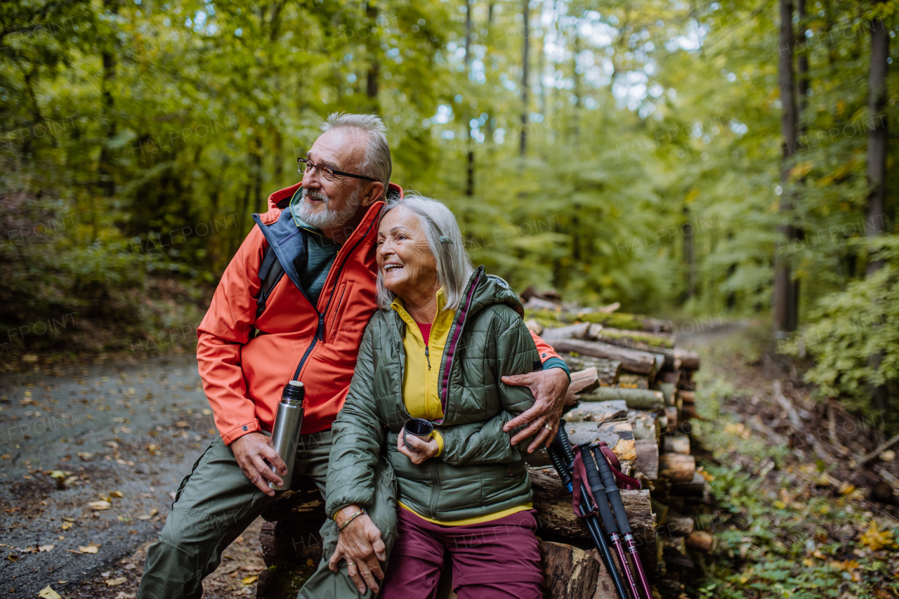 Senior couple having a break during hiking in autumn forest.