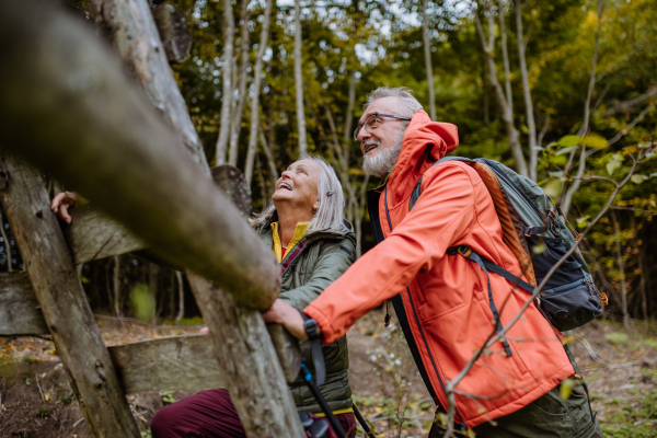 Happy senior couple climbing at hunting high seat in forest.