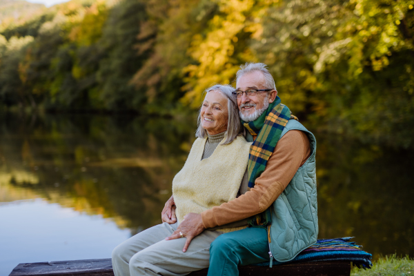 Senior couple in love sitting together on a bench near lake, during autumn day.