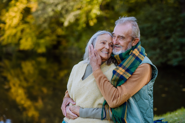 Senior couple in love sitting together on a bench near lake, during autumn day.