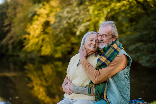 Senior couple in love huging each other near a lake, during autumn day.