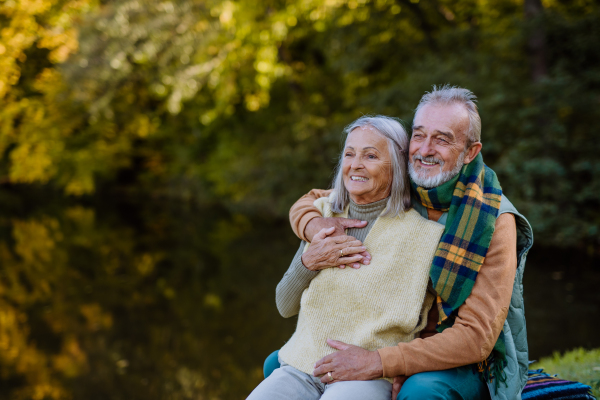 Senior couple in love sitting together on a bench near lake, during autumn day.