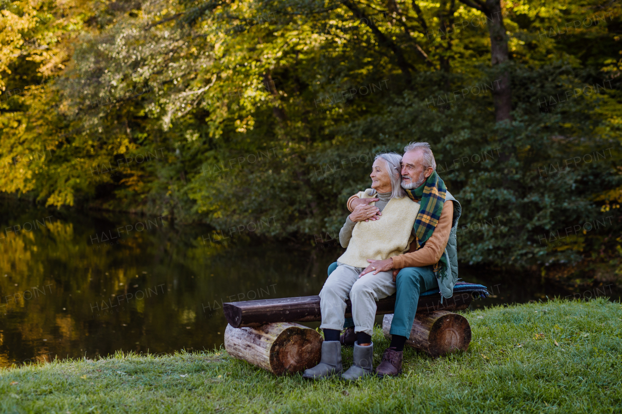 Senior couple in love sitting together on a bench near lake, during autumn day.