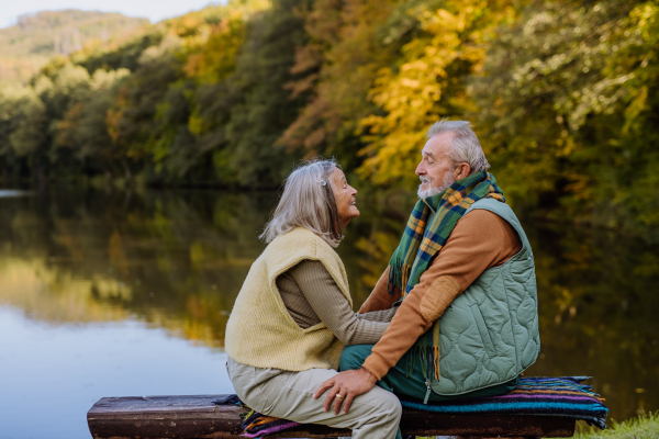 Senior couple in love sitting together on a bench near lake, during autumn day.