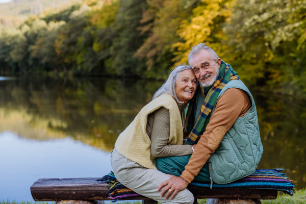 Senior couple in love sitting together on a bench near lake, during autumn day.