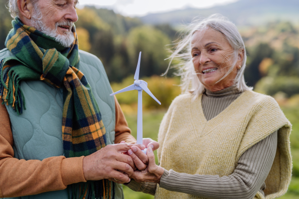 Senior couple holding a plastic model of wind turbine in nature, concept of future, ecology and renewable resources, message for next generation