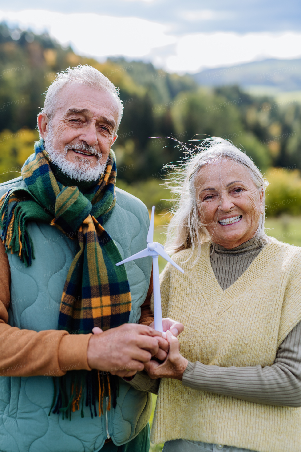 Senior couple holding a plastic model of wind turbine in nature, concept of future, ecology and renewable resources, message for next generation