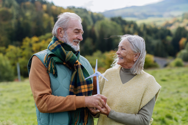 Senior couple holding a plastic model of wind turbine in nature, concept of future, ecology and renewable resources, message for next generation