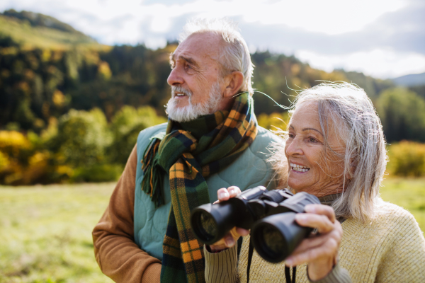 Senior couple looking at view trough a binoculars on autumn walk.