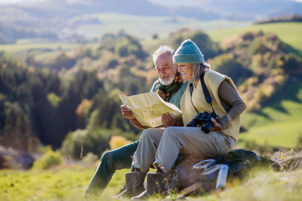 Senior couple having a break, lookig into paper map during hiking in autumn nature.