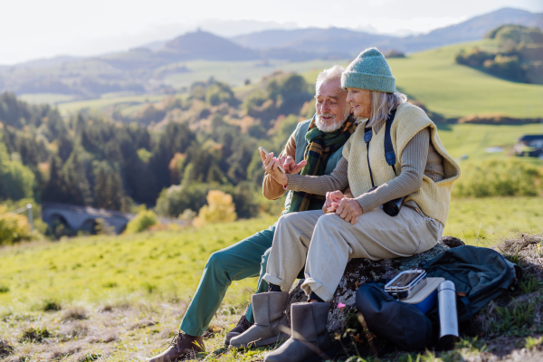 Senior couple having a break, lookig into mobile phone during hiking in autumn nature.